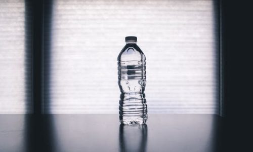 Stylish photo of a clear plastic water bottle on a reflective surface with a soft shadow.