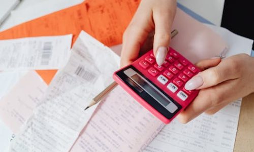 Hands using a pink calculator to manage expenses amidst various receipts and documents.